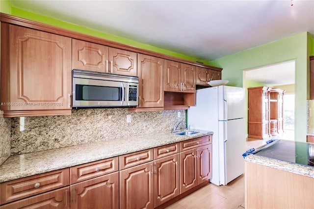 kitchen featuring backsplash, sink, light stone countertops, light wood-type flooring, and white fridge