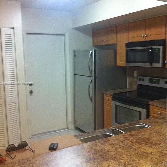 2394 NW 97th Way Unit 2394, Pembroke Pines, FL 33024 - kitchen with stainless steel appliances, brown cabinets, dark countertops, and a sink