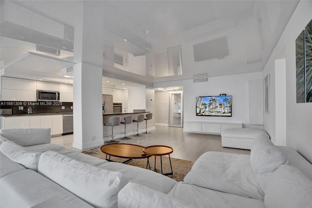 living area with light wood-type flooring, a towering ceiling, and visible vents