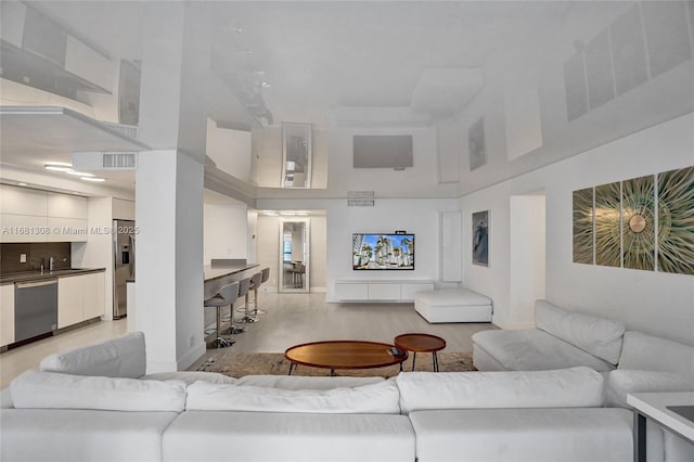 living room with a high ceiling, baseboards, visible vents, and light wood finished floors