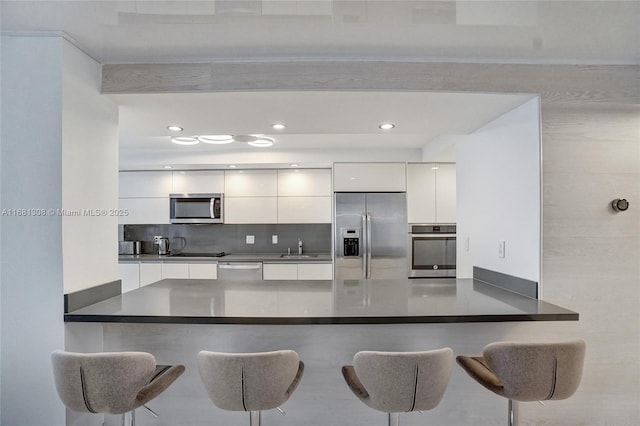 kitchen with dark countertops, appliances with stainless steel finishes, white cabinets, modern cabinets, and a peninsula