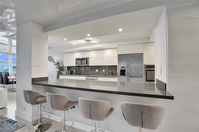 kitchen featuring stainless steel appliances, white cabinets, kitchen peninsula, and tasteful backsplash