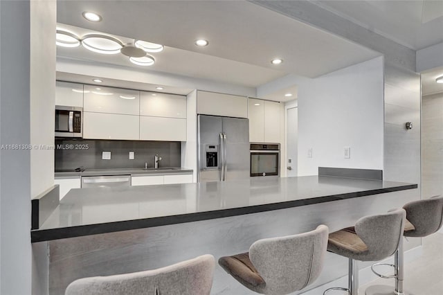 kitchen with a breakfast bar area, stainless steel appliances, white cabinetry, modern cabinets, and a peninsula