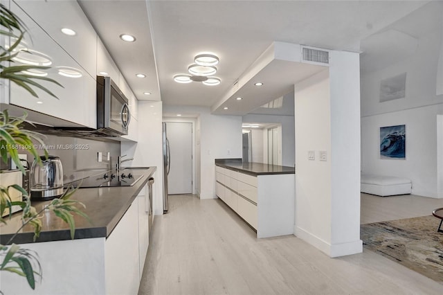 kitchen featuring stainless steel appliances, white cabinets, light wood-type flooring, dark countertops, and modern cabinets