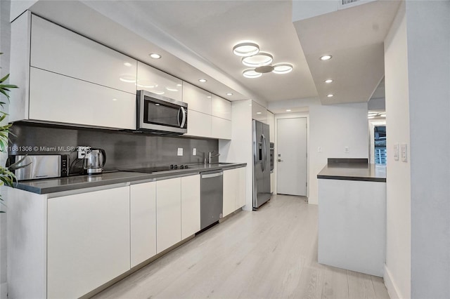 kitchen with stainless steel appliances, light hardwood / wood-style floors, backsplash, and white cabinets