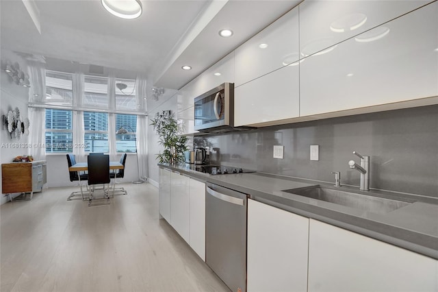 kitchen with light wood-style flooring, a sink, white cabinetry, appliances with stainless steel finishes, and dark countertops