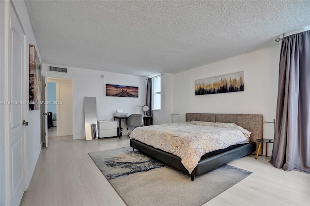 bedroom featuring a textured ceiling, light wood-style flooring, and visible vents