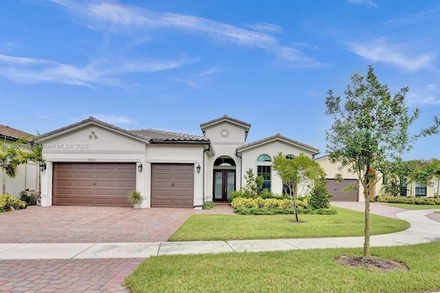 mediterranean / spanish-style home with a tile roof, an attached garage, decorative driveway, a front yard, and stucco siding