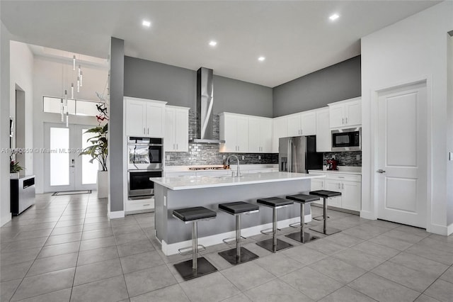 kitchen featuring stainless steel appliances, light countertops, wall chimney range hood, an island with sink, and a kitchen bar