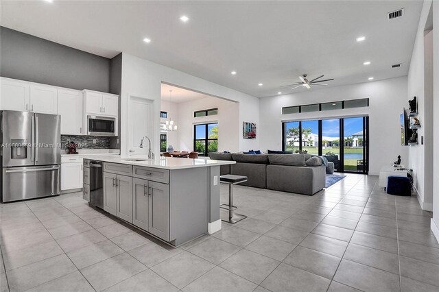 kitchen with stainless steel appliances, white cabinets, an island with sink, a kitchen breakfast bar, and wall chimney range hood