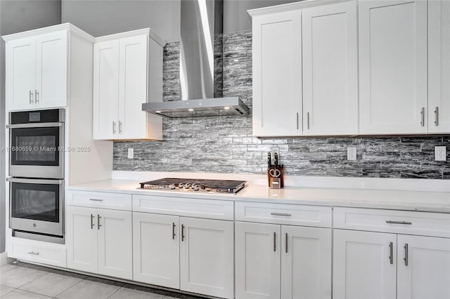 kitchen with stainless steel appliances, white cabinets, light countertops, and wall chimney range hood