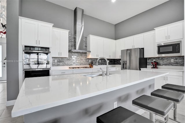 kitchen with stainless steel appliances, white cabinetry, sink, wall chimney exhaust hood, and a breakfast bar area