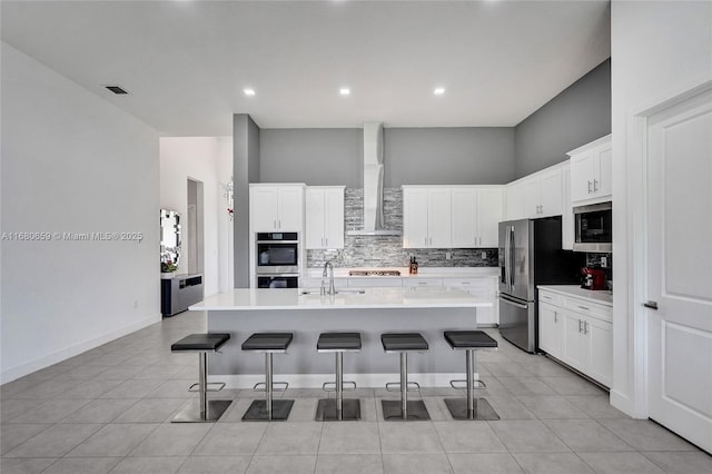 kitchen featuring a kitchen bar, light countertops, wall chimney range hood, and an island with sink