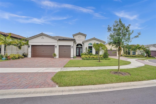 mediterranean / spanish-style home featuring a tiled roof, an attached garage, decorative driveway, a front lawn, and stucco siding