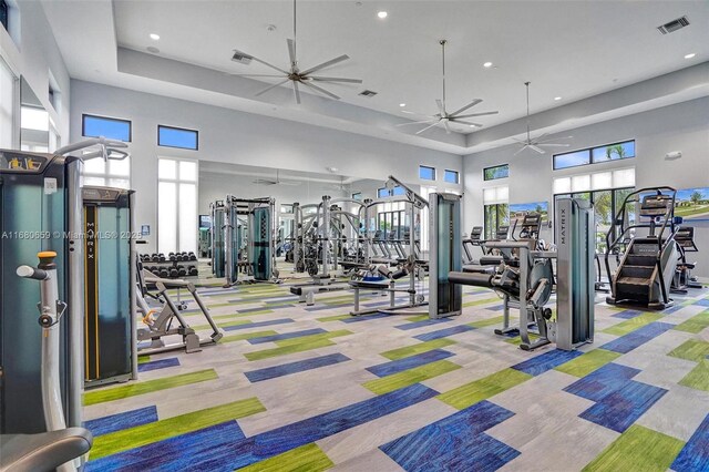 exercise room featuring a raised ceiling, ceiling fan, and a towering ceiling