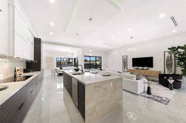 kitchen with light stone counters, decorative light fixtures, a center island with sink, and white cabinets