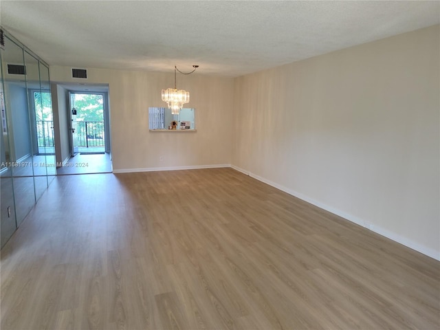 unfurnished room featuring hardwood / wood-style flooring, a textured ceiling, and an inviting chandelier