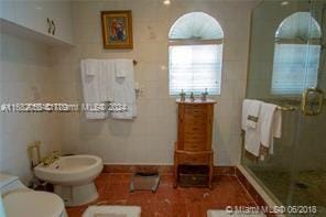 bathroom featuring tile walls, a shower with shower door, a bidet, and toilet