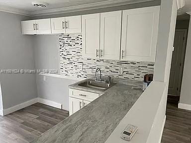 kitchen featuring white cabinets, backsplash, ornamental molding, dark wood-type flooring, and sink