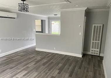 spare room with an AC wall unit, ornamental molding, and dark wood-type flooring