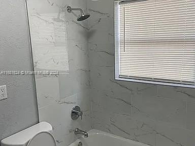 bathroom with toilet and tiled shower / bath