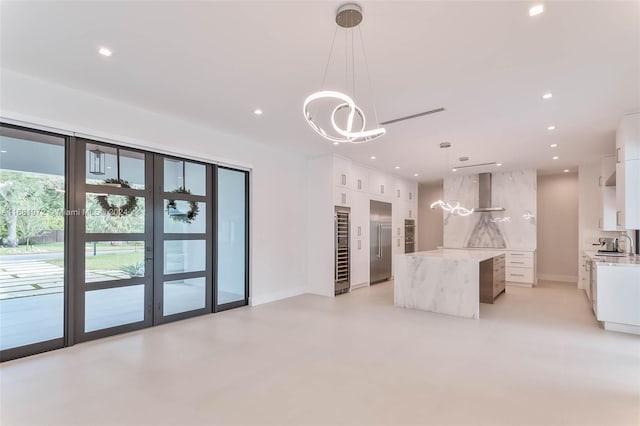 kitchen featuring hanging light fixtures, white cabinetry, sink, wall chimney exhaust hood, and a center island