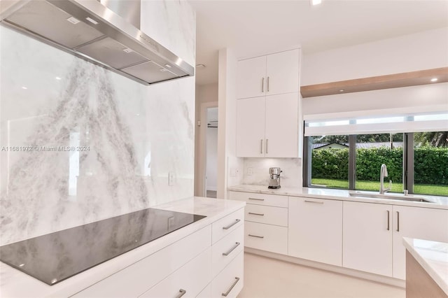 kitchen featuring black electric stovetop, sink, white cabinetry, wall chimney exhaust hood, and light stone counters