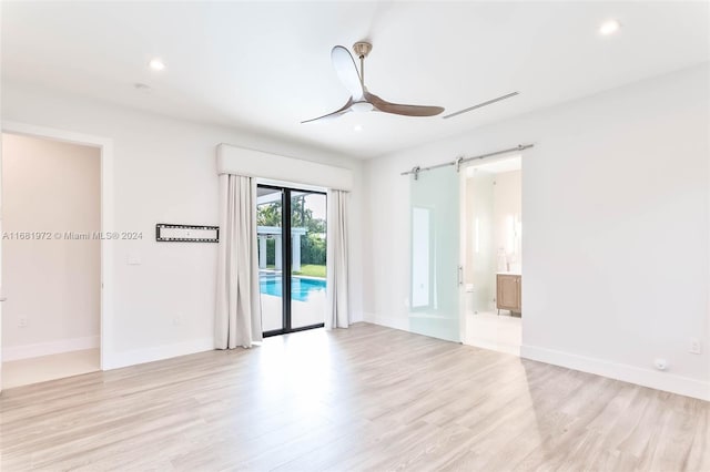 spare room with ceiling fan, light hardwood / wood-style flooring, and a barn door