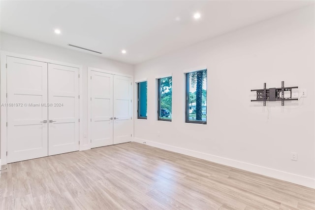 unfurnished bedroom with light hardwood / wood-style floors and multiple closets