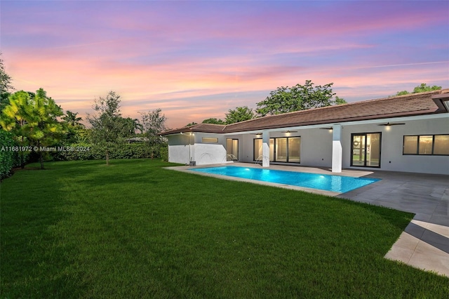 pool at dusk with a patio area and a lawn