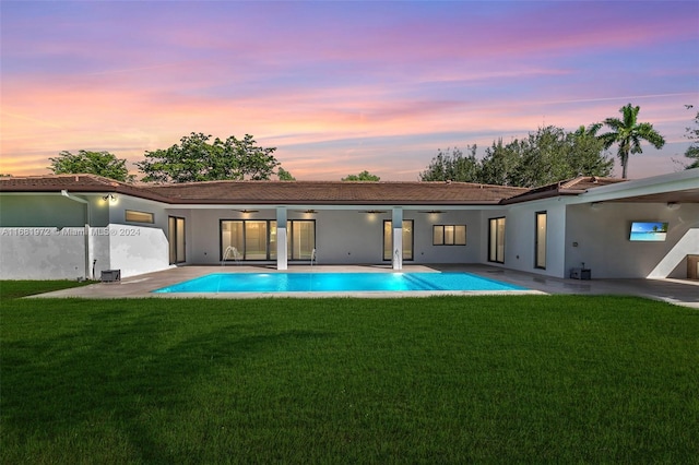 7720 SW 130th St, Pinecrest, FL 33156 - back of house at dusk featuring a patio area, an outdoor pool, a ceiling fan, a yard, and stucco siding