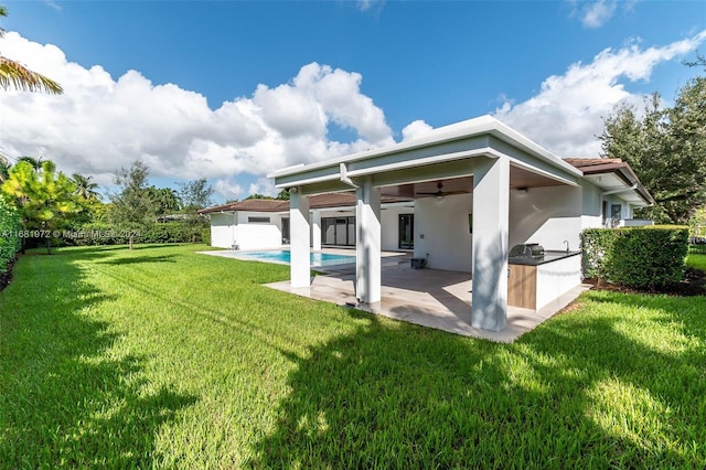 back of property with exterior kitchen, a lawn, a patio area, a fenced in pool, and ceiling fan