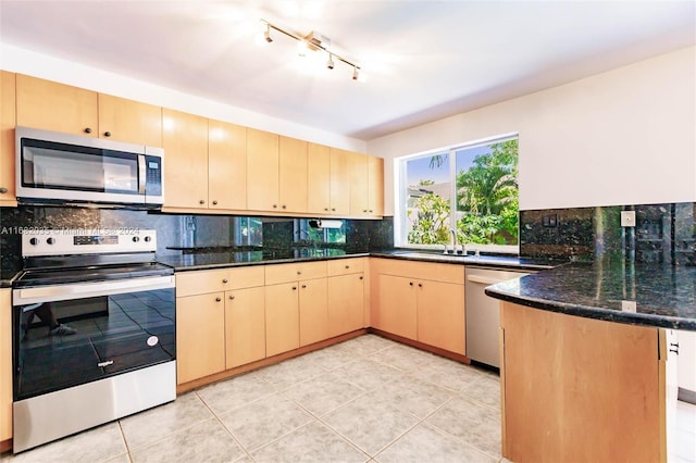 kitchen featuring light brown cabinets, kitchen peninsula, dark stone counters, decorative backsplash, and appliances with stainless steel finishes