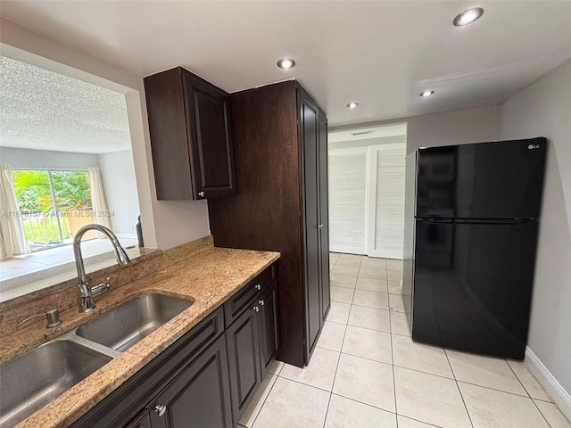 kitchen featuring black refrigerator, sink, light stone countertops, dark brown cabinetry, and light tile patterned floors