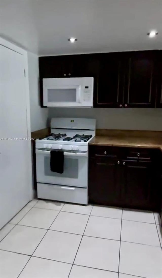 kitchen with dark brown cabinetry, light tile patterned floors, and white appliances