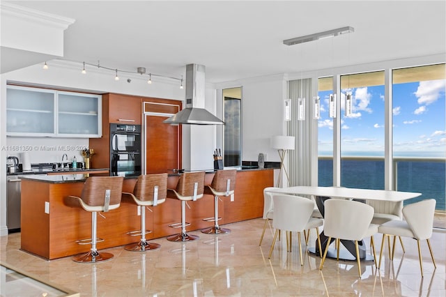 kitchen featuring a water view, a breakfast bar area, exhaust hood, and black double oven