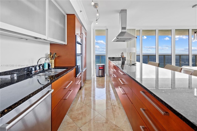 kitchen featuring appliances with stainless steel finishes, dark stone countertops, wall chimney exhaust hood, sink, and a water view