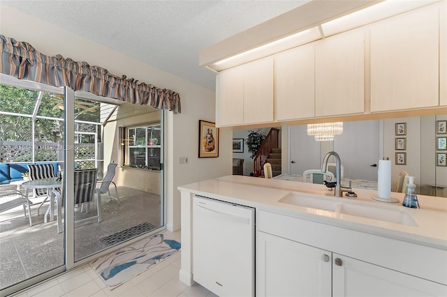 kitchen featuring white dishwasher, sink, light tile patterned flooring, white cabinets, and a textured ceiling