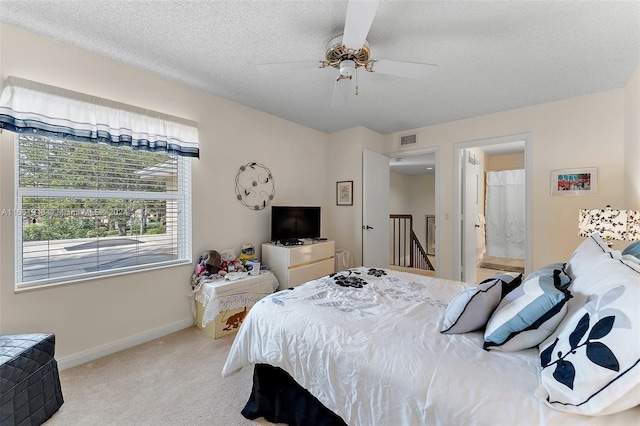 carpeted bedroom with a textured ceiling, ensuite bath, and ceiling fan