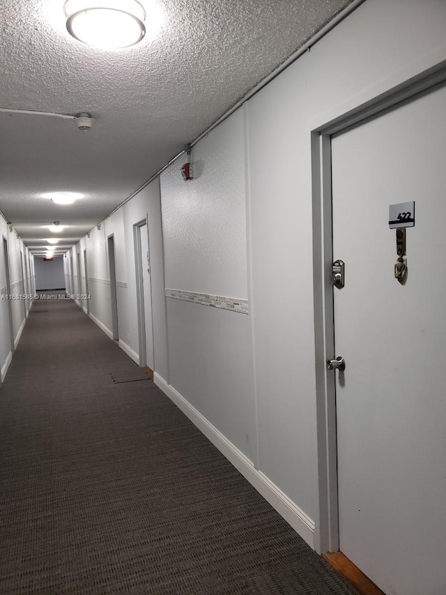 hall featuring a textured ceiling and dark carpet