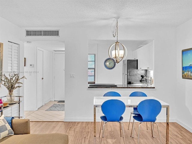 dining space featuring a textured ceiling, an inviting chandelier, and light wood-type flooring