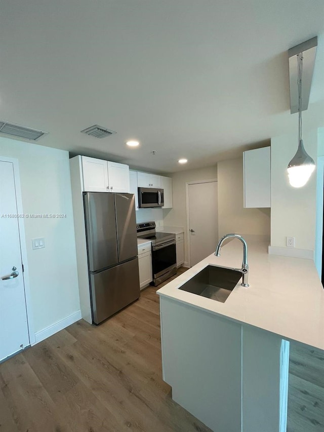 kitchen with kitchen peninsula, hanging light fixtures, appliances with stainless steel finishes, white cabinetry, and sink