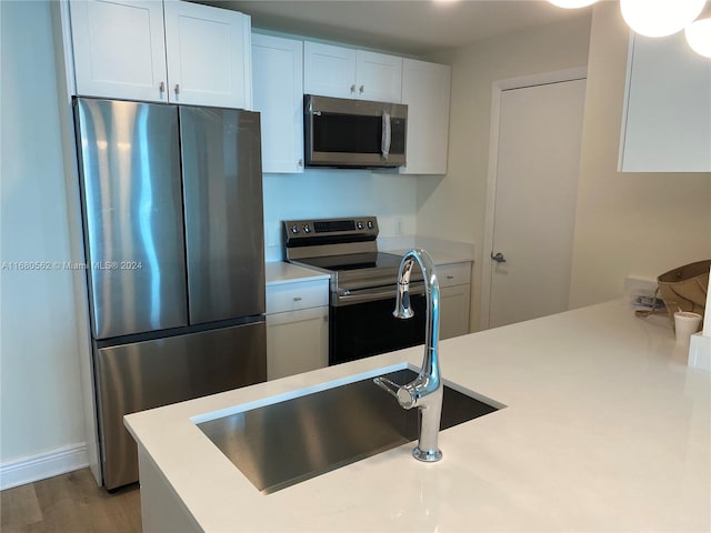 kitchen with appliances with stainless steel finishes, white cabinetry, sink, and wood-type flooring