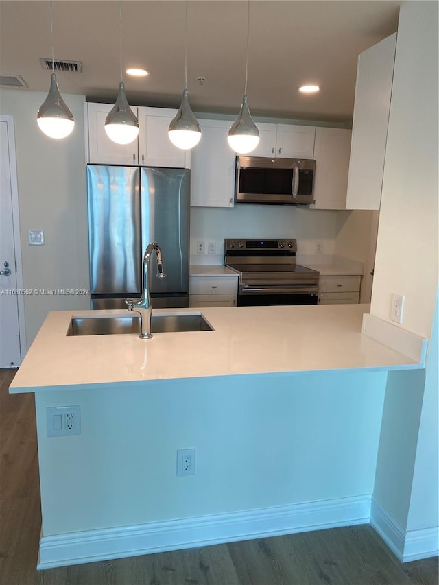 kitchen with appliances with stainless steel finishes, sink, hanging light fixtures, white cabinets, and dark wood-type flooring