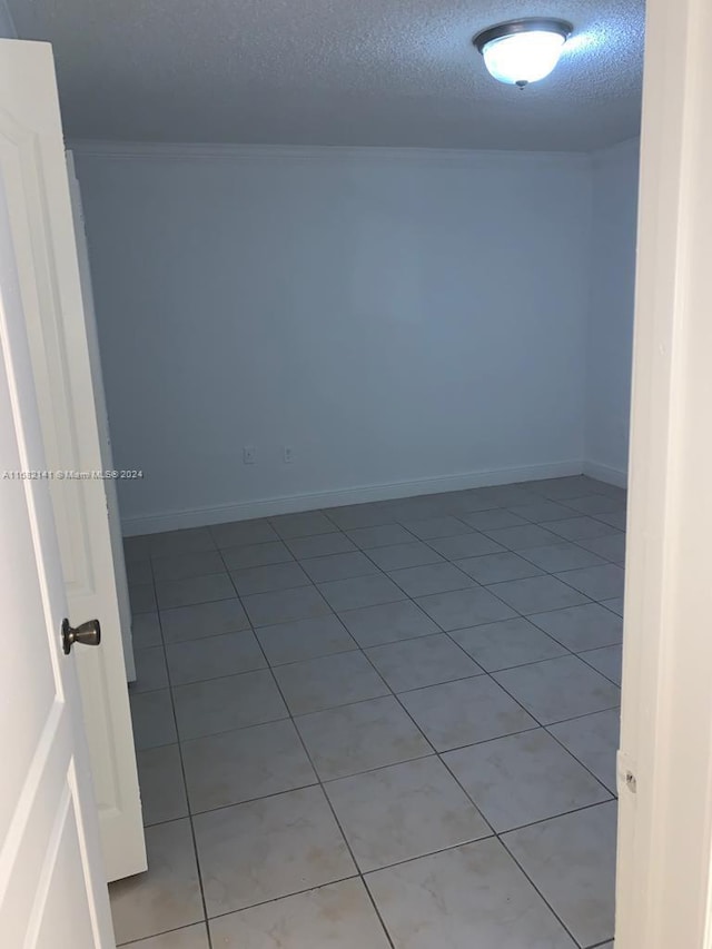 unfurnished room with crown molding, a textured ceiling, and light tile patterned floors