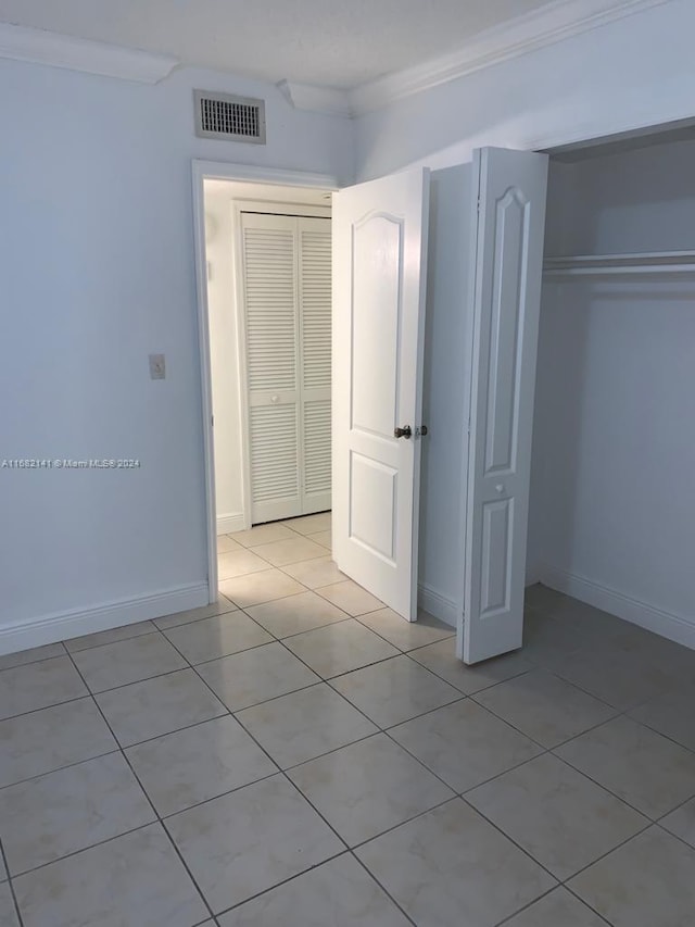 unfurnished bedroom featuring a closet, crown molding, and light tile patterned floors