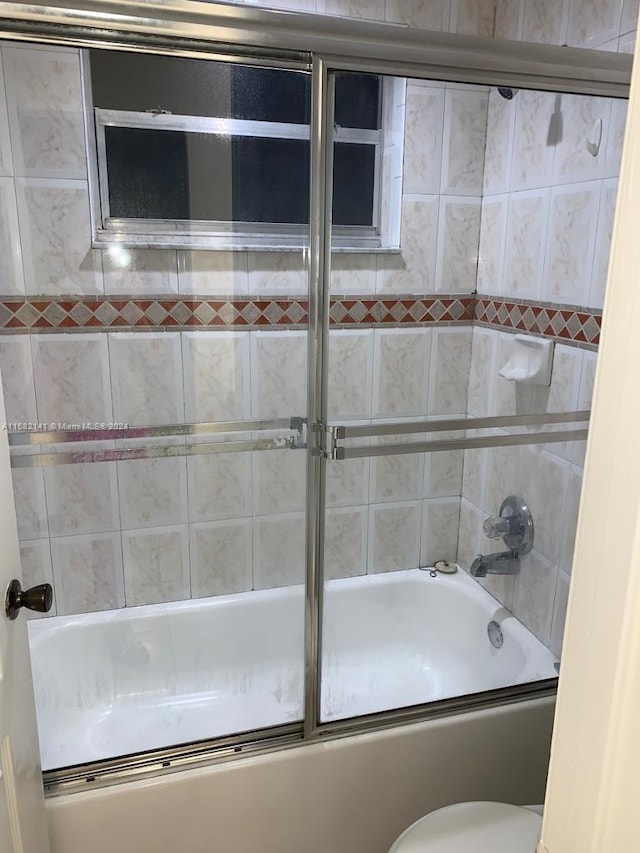 bathroom featuring toilet and bath / shower combo with glass door