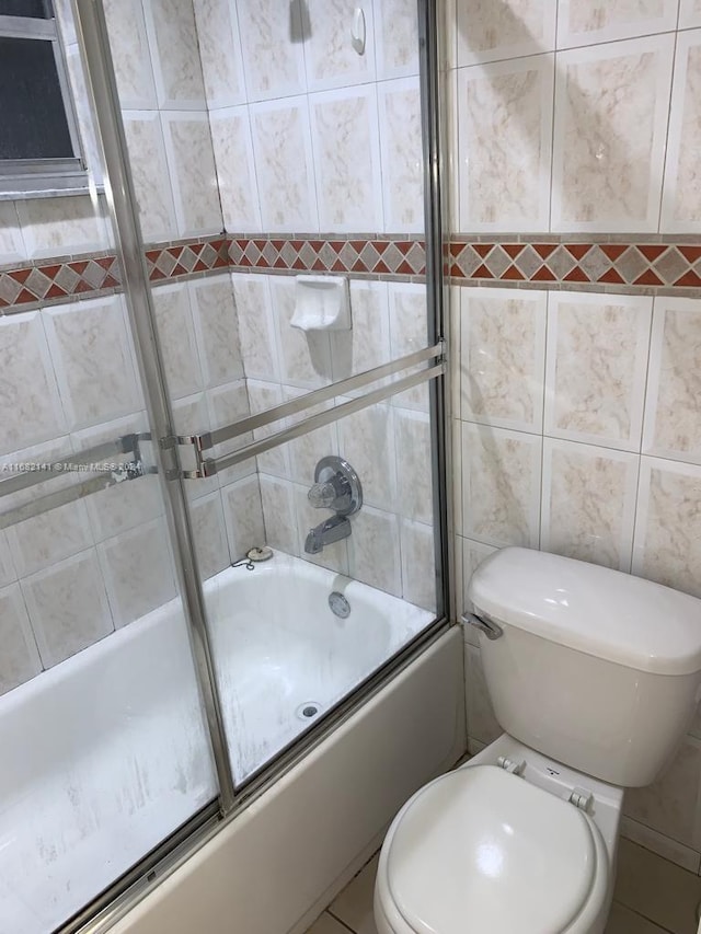 bathroom with toilet, combined bath / shower with glass door, tile patterned floors, and tile walls