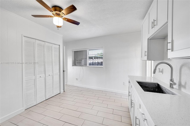 kitchen featuring white cabinets, sink, ceiling fan, a textured ceiling, and light stone counters