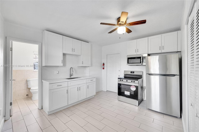 kitchen featuring stainless steel appliances, ceiling fan, sink, light tile patterned floors, and white cabinets